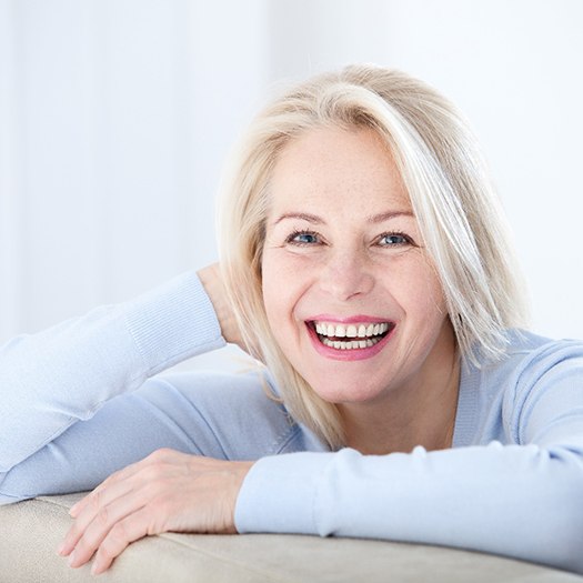 Senior woman in light blue shirt leaning on couch 