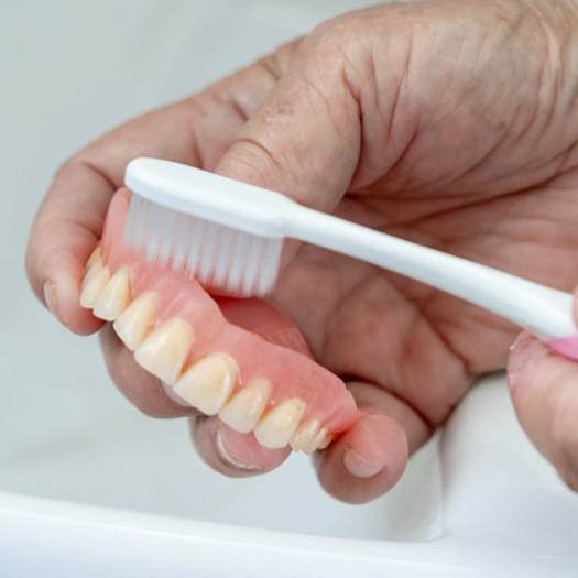Patient carefully brushing their denture