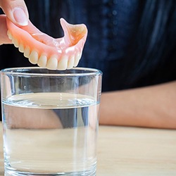 Patient dropping their denture into a cleaning solution to soak