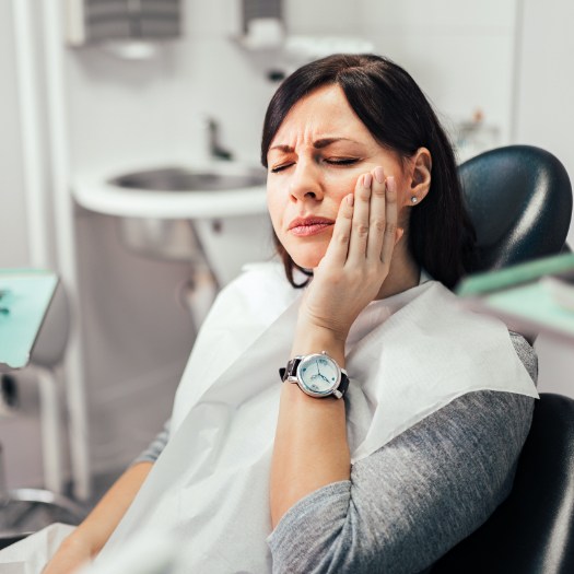 Woman in dental chair for emergency dentistry holding cheek