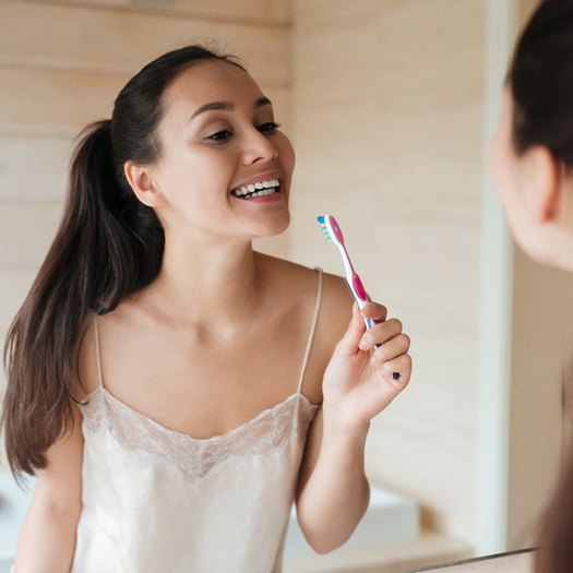 Woman smiling in mirror and holding toothbrush