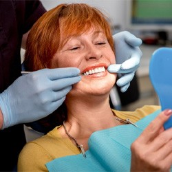 An older woman admiring her dental implants in a hand mirror