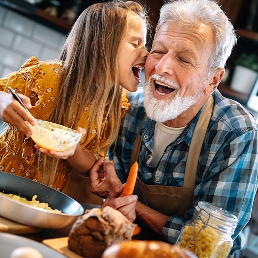 Older man with dental implant supported replacement teeth laughing with granddaughter