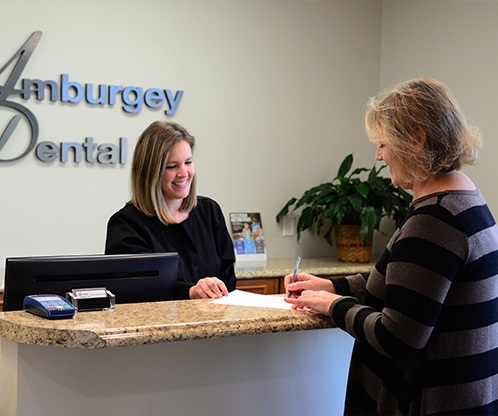 Smiling dental team member greeting patient at reception desk
