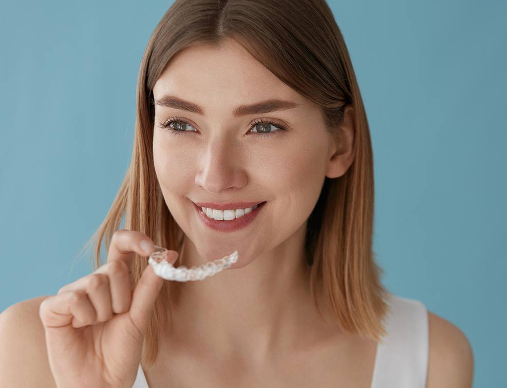A young woman with blonde hair preparing to insert a clear aligner that is part of her treatment with Invisalign in Abingdon