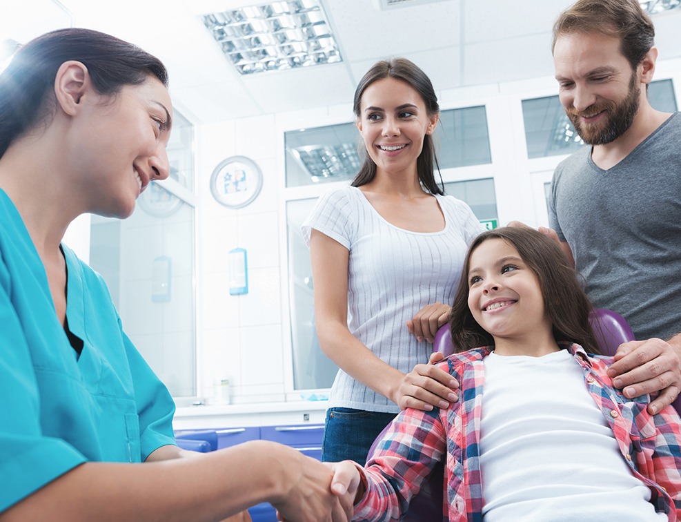 Young girl and parent smiling at dental team member during children's dentistry visit