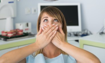 Woman afraid of the dentist in need of sedation dentistry covering her mouth