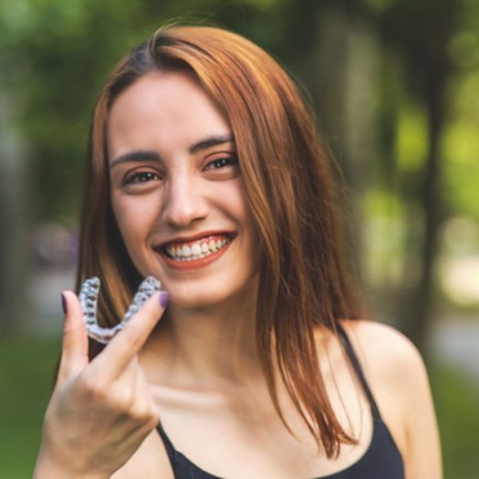 Woman holding dental aligner, enjoying benefits of SureSmile